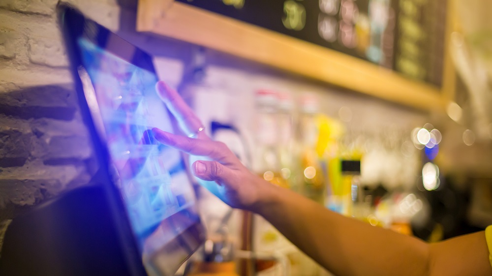 Blurry picture of cashier is making order on touch screen of computer in cafe or store. Barista is using the screen to receive orders from customers who are pointing to order coffee.
