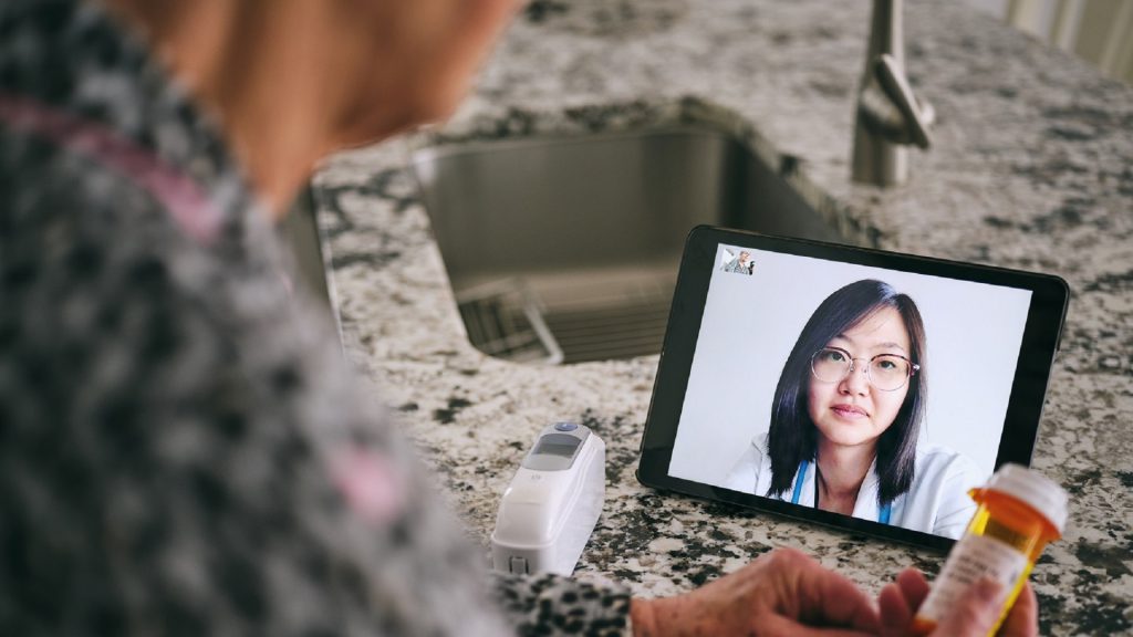 A senior aged woman in her home, talking to a doctor online in a virtual appointment.